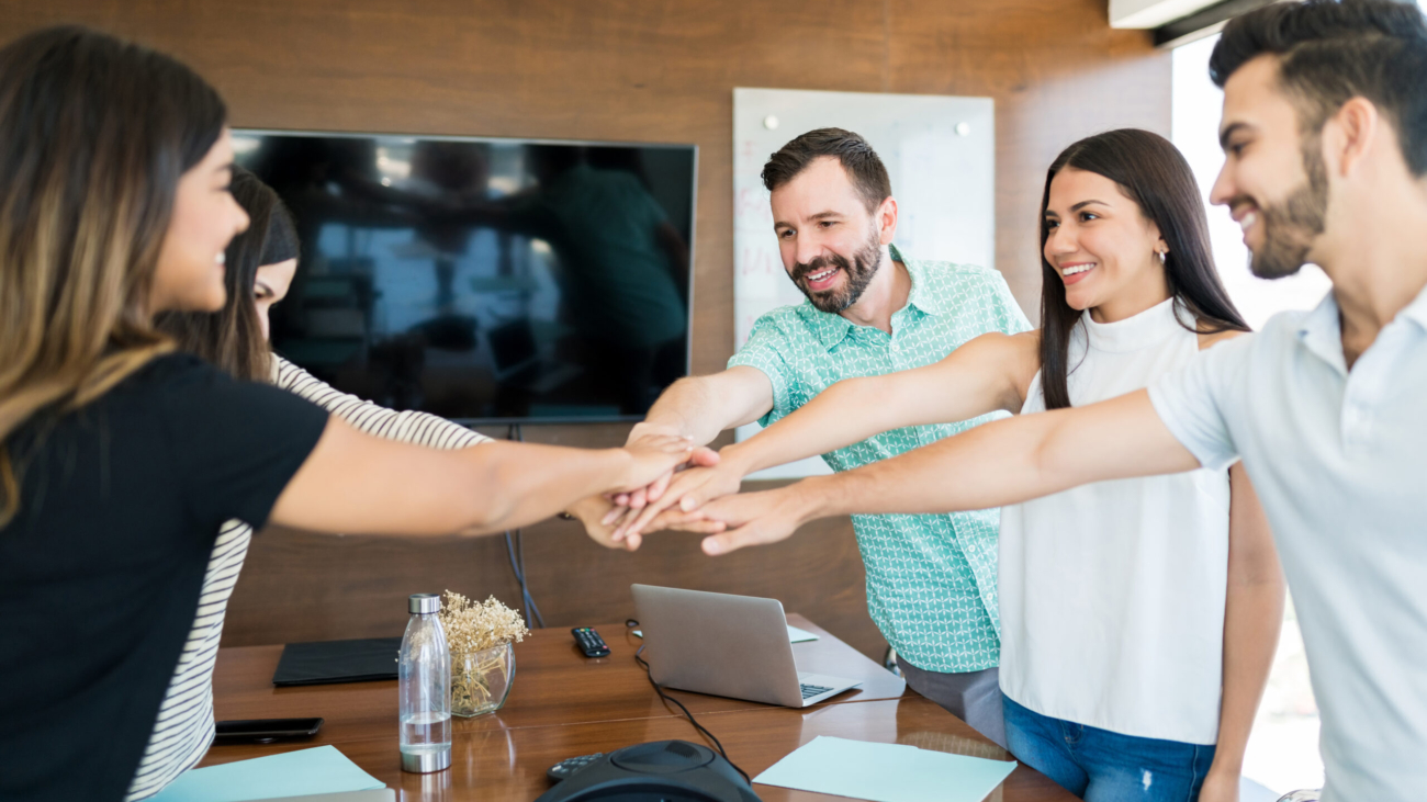 Smiling business colleagues with their hands stacked over table in meeting at office