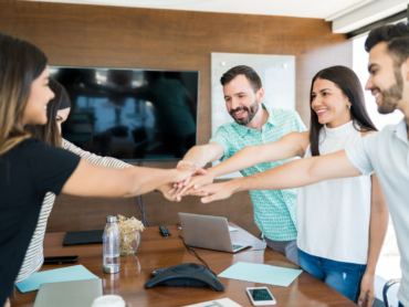 Smiling business colleagues with their hands stacked over table in meeting at office
