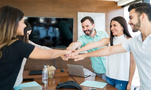Smiling business colleagues with their hands stacked over table in meeting at office